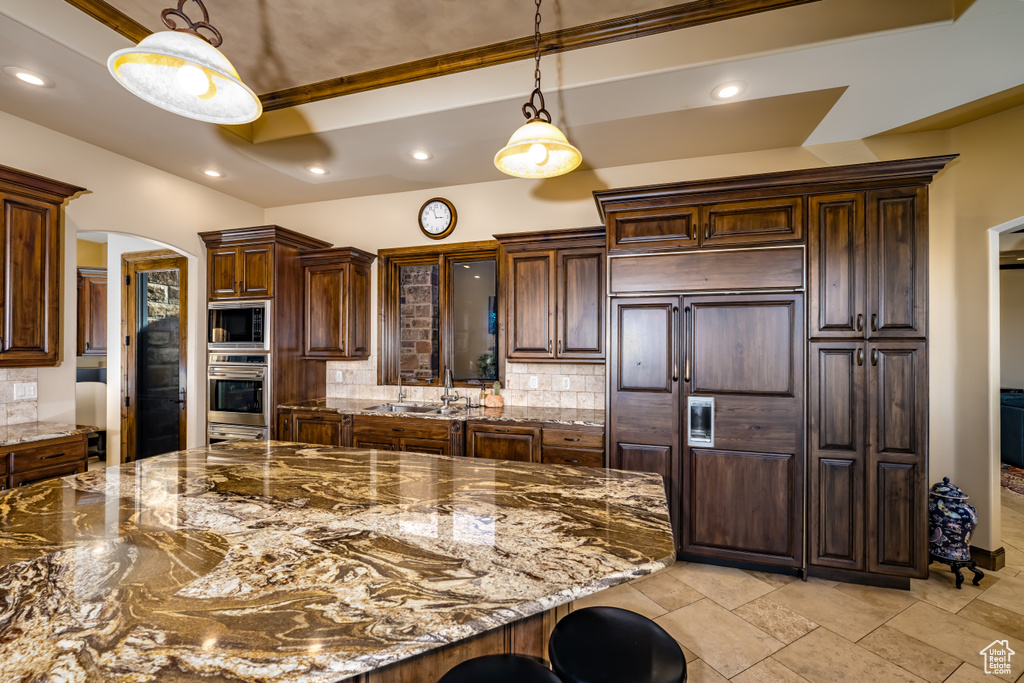 Kitchen featuring hanging light fixtures, a kitchen bar, decorative backsplash, dark stone countertops, and dark brown cabinets