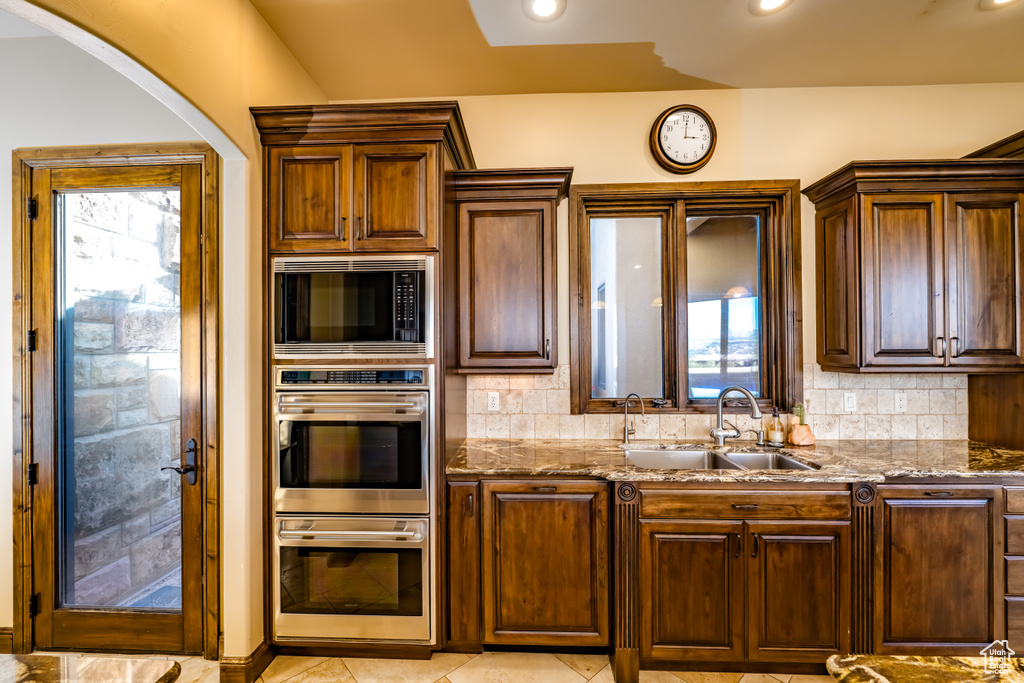 Kitchen with built in microwave, stainless steel double oven, sink, stone countertops, and backsplash