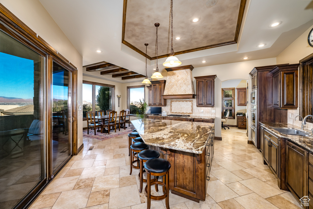 Kitchen featuring sink, a spacious island, custom exhaust hood, a tray ceiling, and crown molding