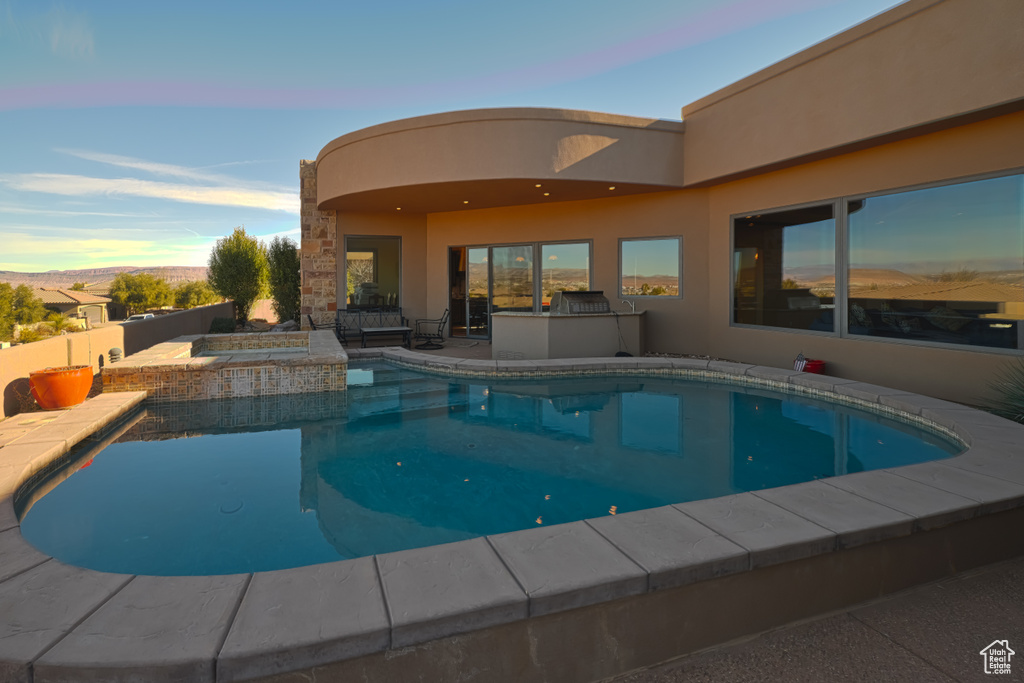 Pool at dusk featuring an in ground hot tub and a patio area