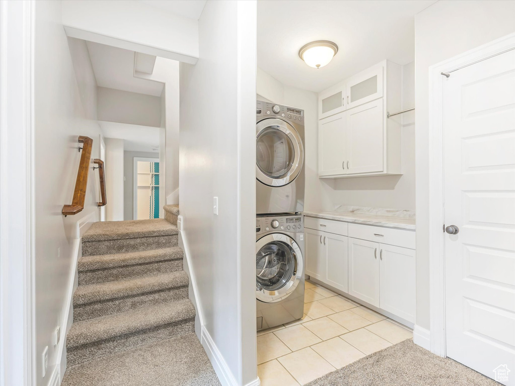 Laundry room featuring stacked washer and dryer, cabinets, and light tile patterned flooring