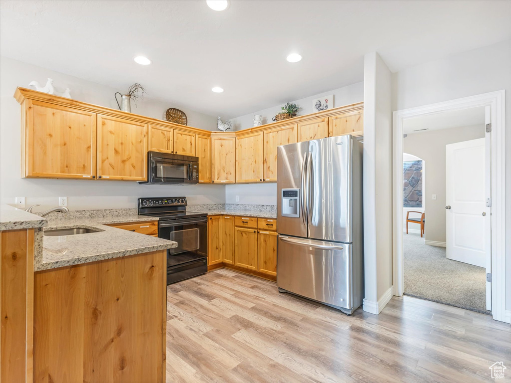 Kitchen featuring light stone countertops, kitchen peninsula, light hardwood / wood-style flooring, black appliances, and sink
