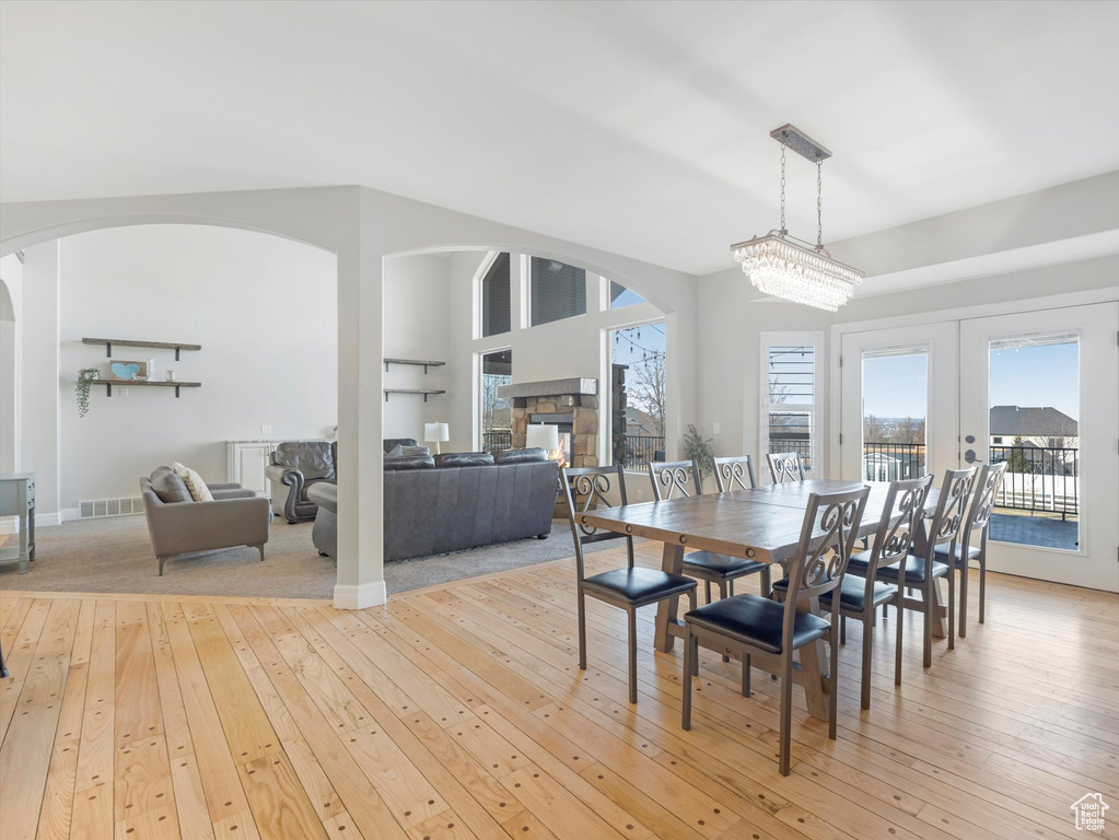 Dining space with a notable chandelier, light wood-type flooring, french doors, and a stone fireplace