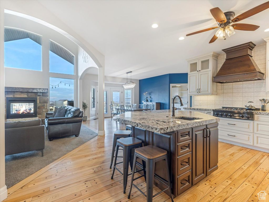 Kitchen with sink, white cabinets, stainless steel gas cooktop, premium range hood, and a center island with sink