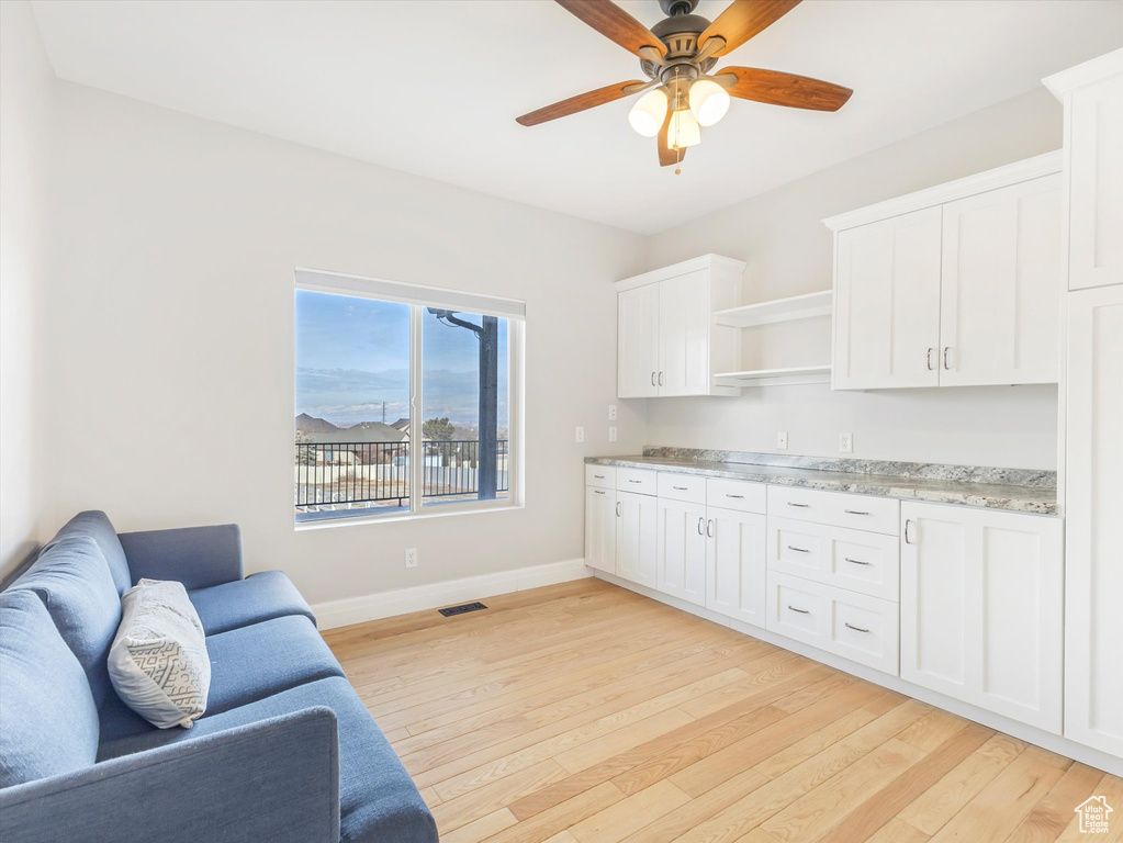 Kitchen featuring light stone counters, ceiling fan, white cabinetry, and light wood-type flooring