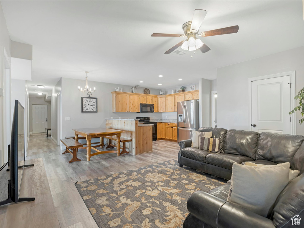 Living room with ceiling fan with notable chandelier and light hardwood / wood-style floors