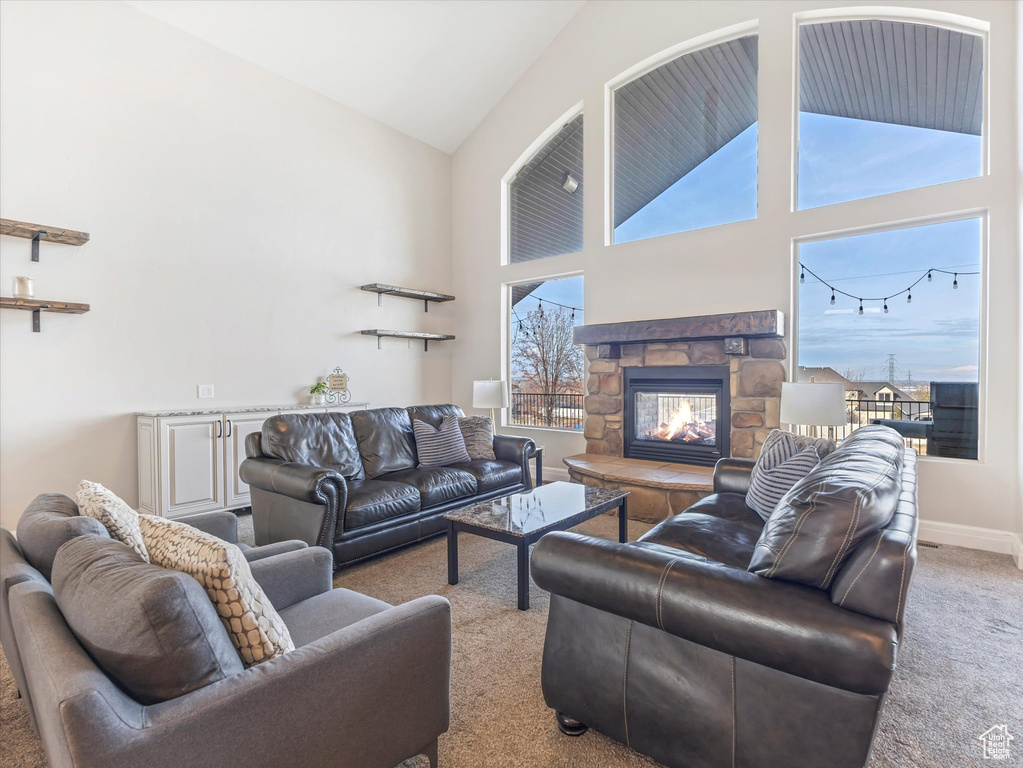 Living room featuring a wealth of natural light, light colored carpet, a stone fireplace, and high vaulted ceiling