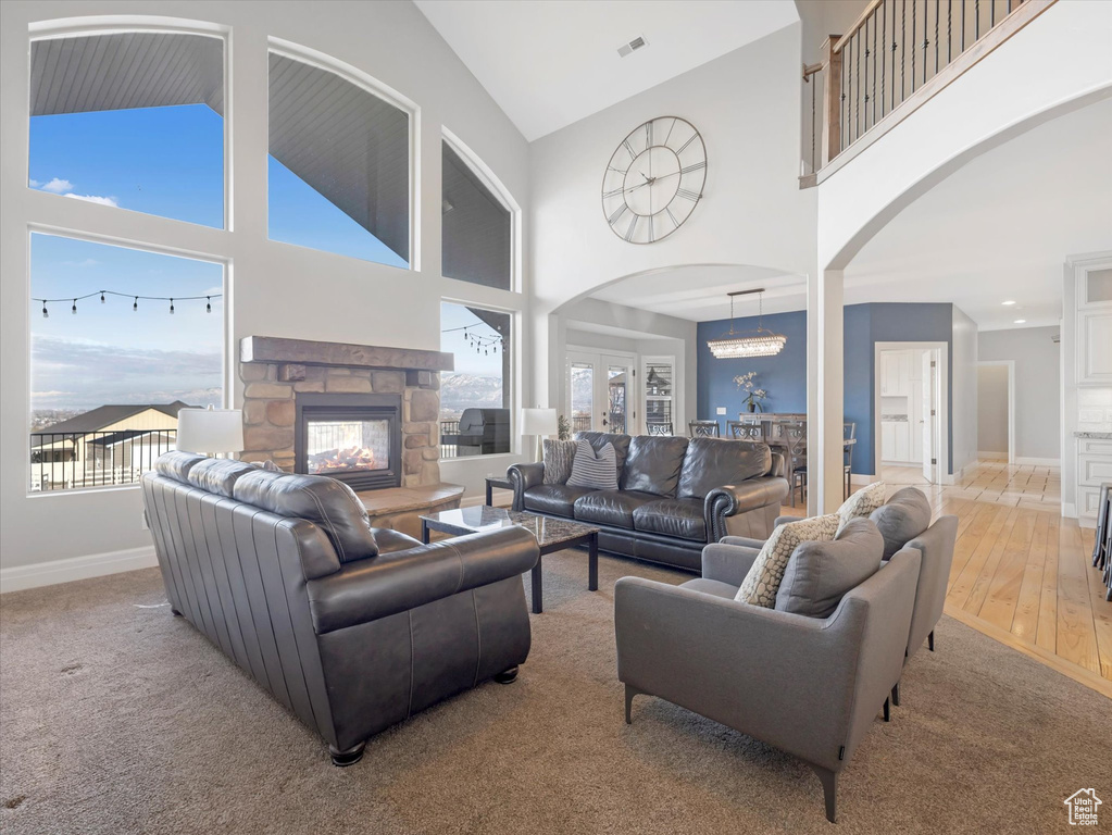 Carpeted living room with a notable chandelier, a stone fireplace, and high vaulted ceiling
