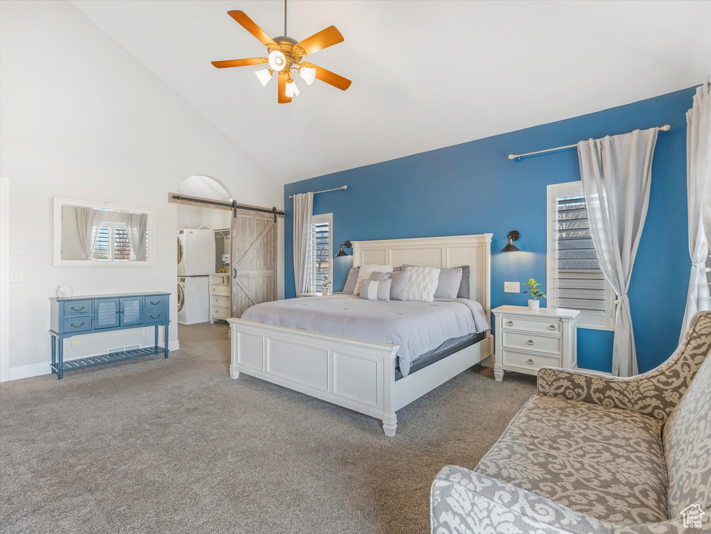 Carpeted bedroom featuring high vaulted ceiling, multiple windows, ceiling fan, and a barn door