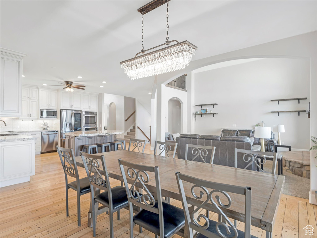Dining room with ceiling fan with notable chandelier, sink, and light hardwood / wood-style floors