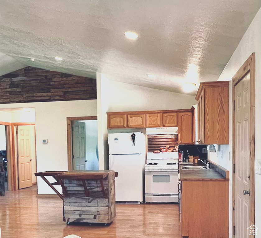 Kitchen featuring vaulted ceiling, a textured ceiling, light wood-type flooring, and white appliances