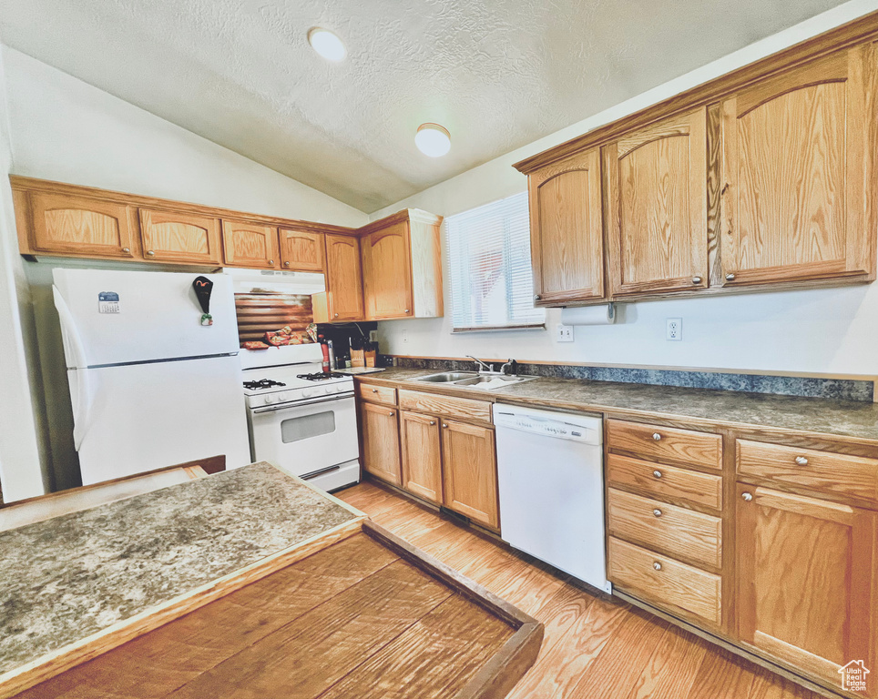 Kitchen with white appliances, a textured ceiling, light hardwood / wood-style floors, sink, and vaulted ceiling