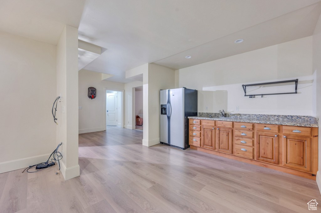 Kitchen featuring light stone countertops, sink, stainless steel refrigerator with ice dispenser, and light wood-type flooring