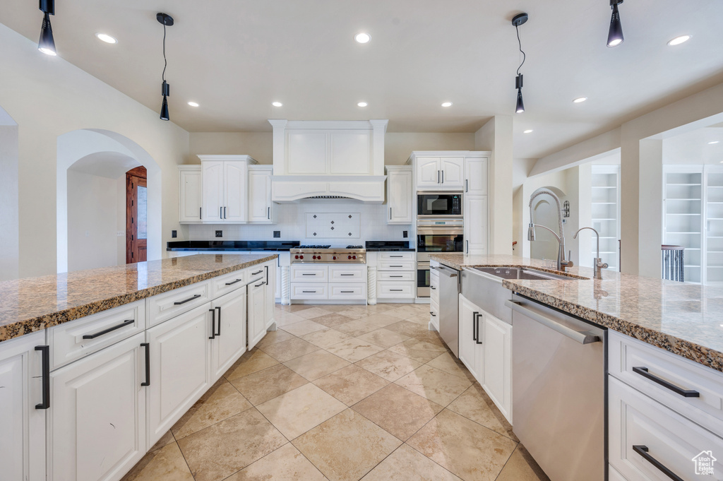 Kitchen with hanging light fixtures, decorative backsplash, appliances with stainless steel finishes, light stone counters, and white cabinetry