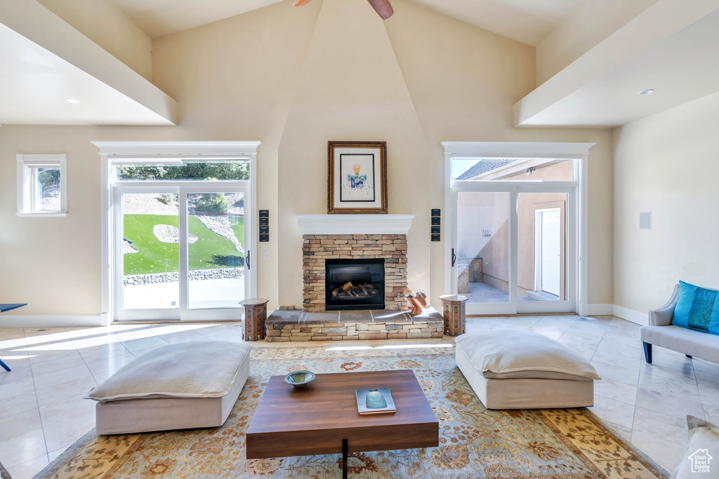 Tiled living room featuring a high ceiling, a stone fireplace, and ceiling fan