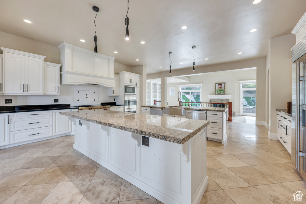 Kitchen featuring white cabinetry, a large island, dark stone counters, decorative light fixtures, and appliances with stainless steel finishes