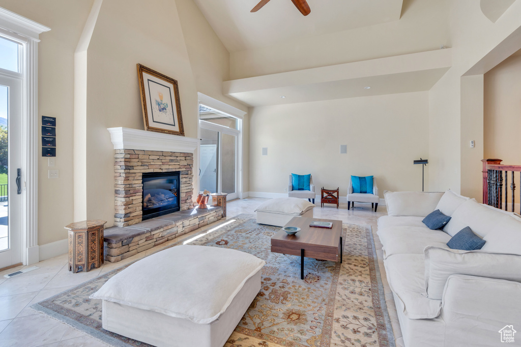 Living room with a fireplace, a towering ceiling, ceiling fan, and light tile patterned flooring