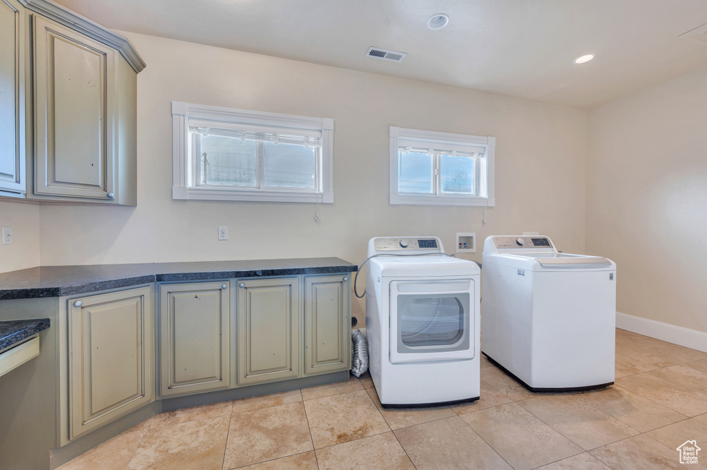 Clothes washing area featuring light tile patterned floors, cabinets, and independent washer and dryer