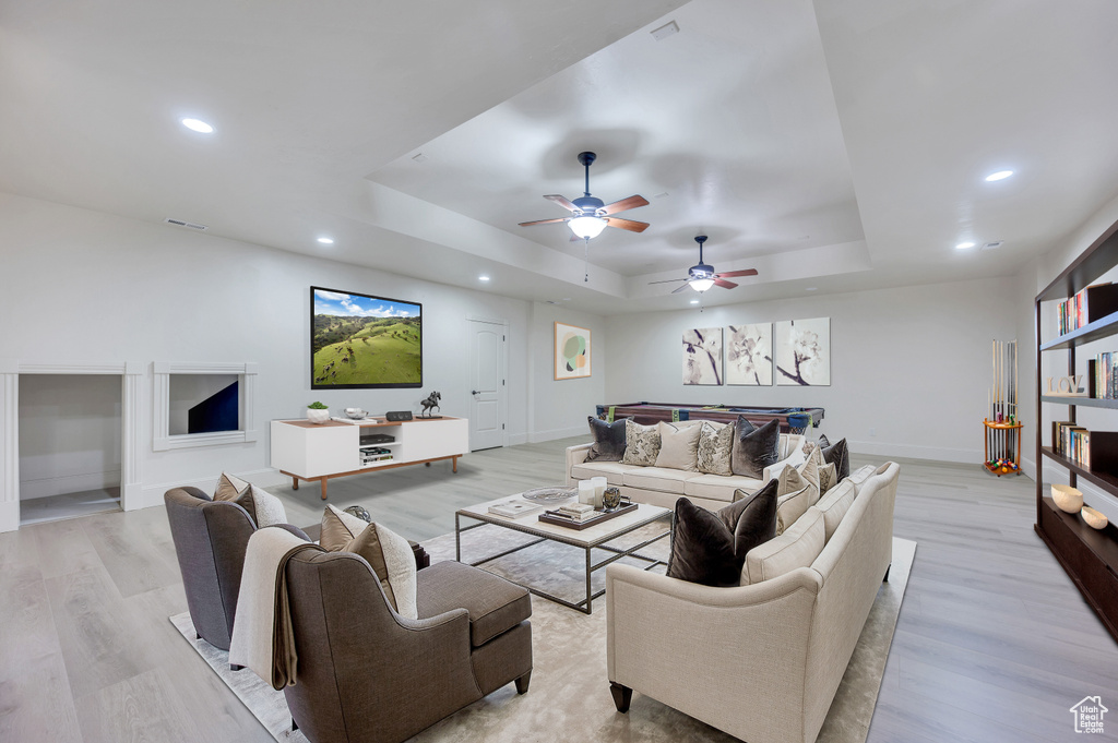 Living room with a tray ceiling, ceiling fan, and light hardwood / wood-style floors