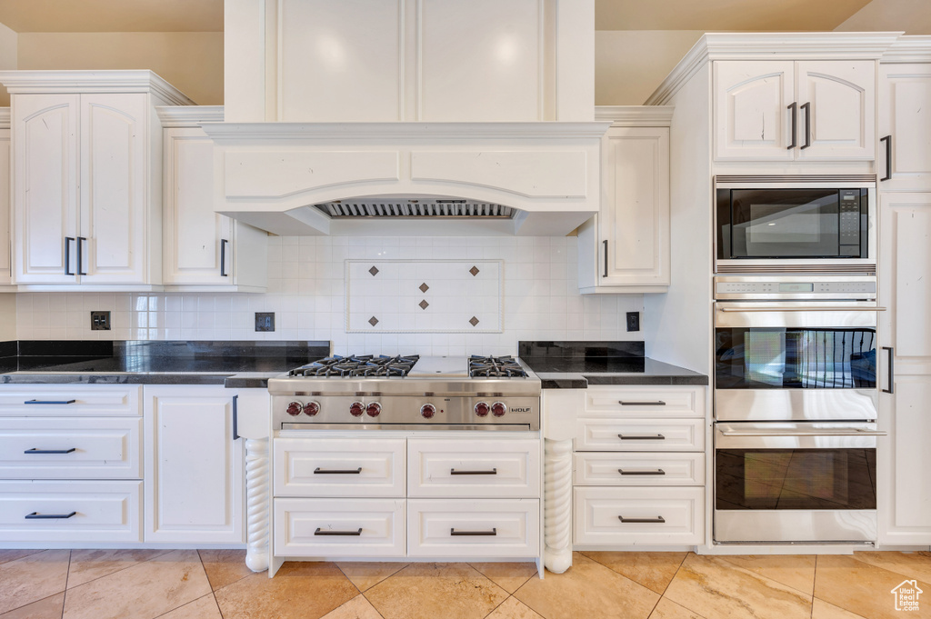 Kitchen featuring white cabinets, custom range hood, backsplash, and stainless steel appliances