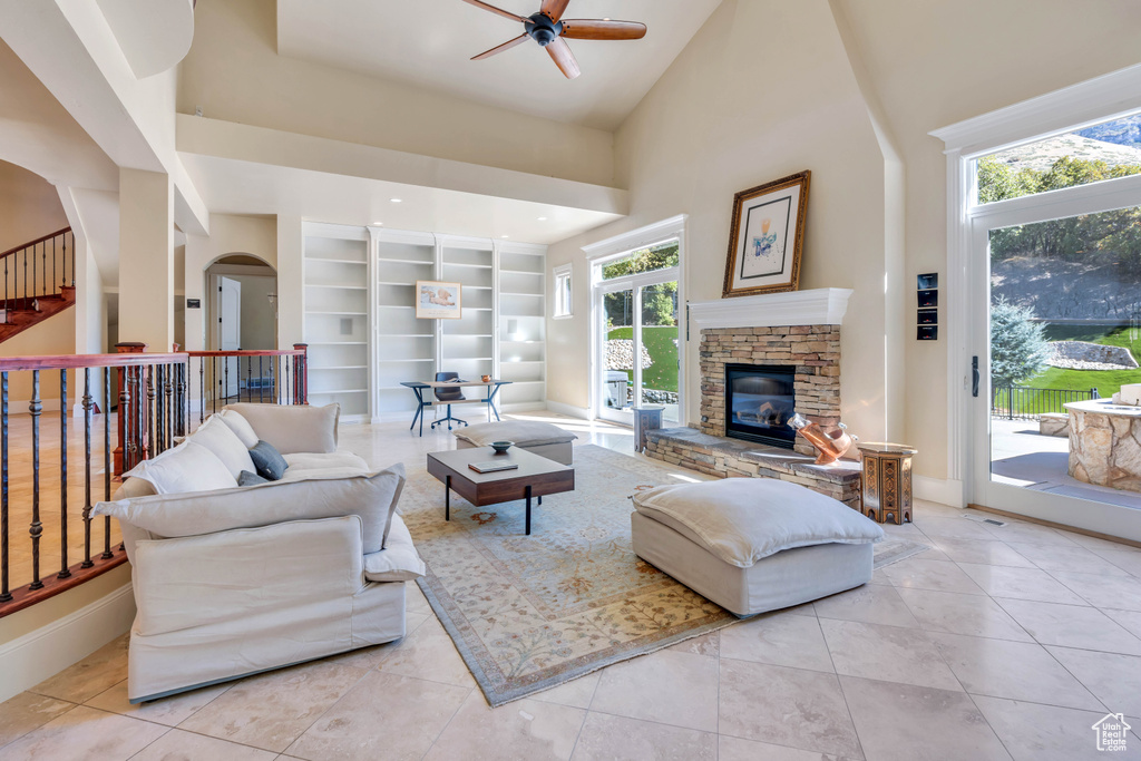 Tiled living room featuring built in shelves, ceiling fan, a fireplace, and high vaulted ceiling