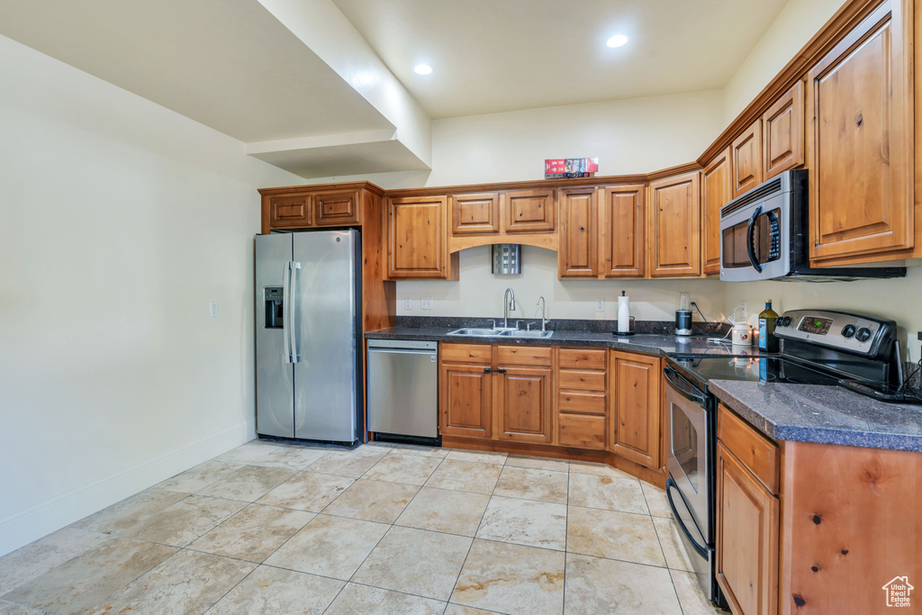 Kitchen with dark stone countertops, light tile patterned floors, sink, and appliances with stainless steel finishes