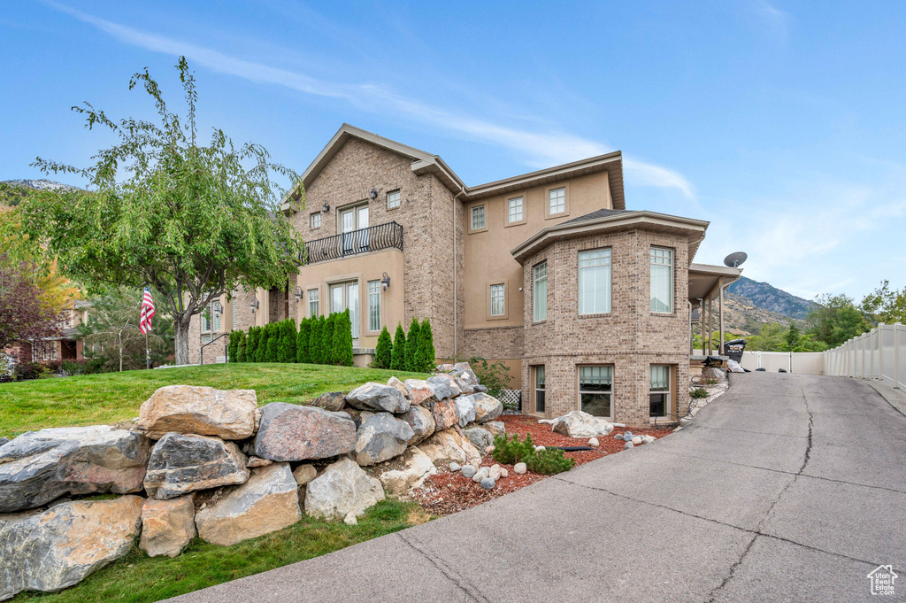 View of front of home with a mountain view, a balcony, and a front yard