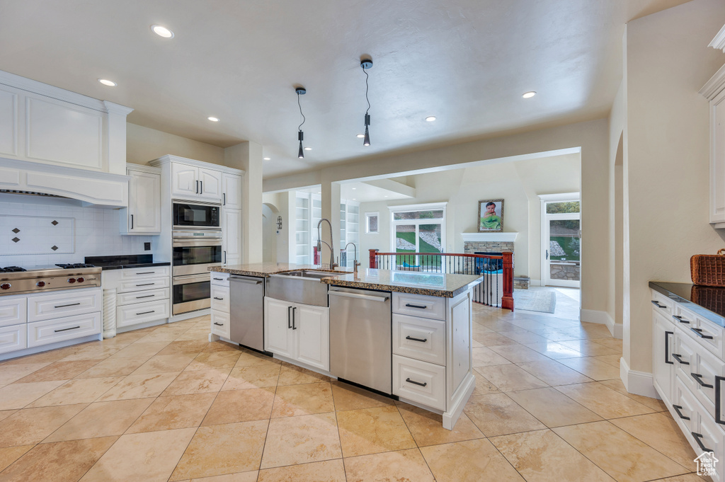 Kitchen with sink, a fireplace, white cabinets, a center island with sink, and appliances with stainless steel finishes