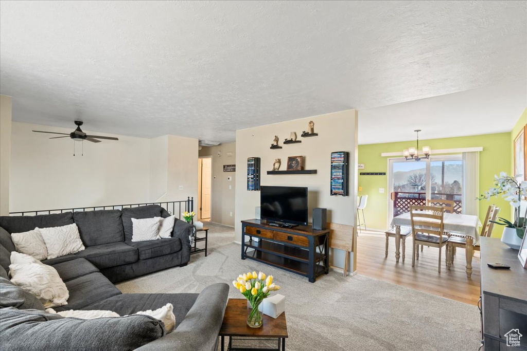 Carpeted living room with ceiling fan with notable chandelier and a textured ceiling