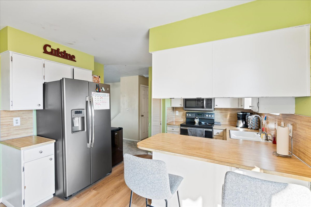 Kitchen with kitchen peninsula, decorative backsplash, sink, stainless steel appliances, and white cabinets