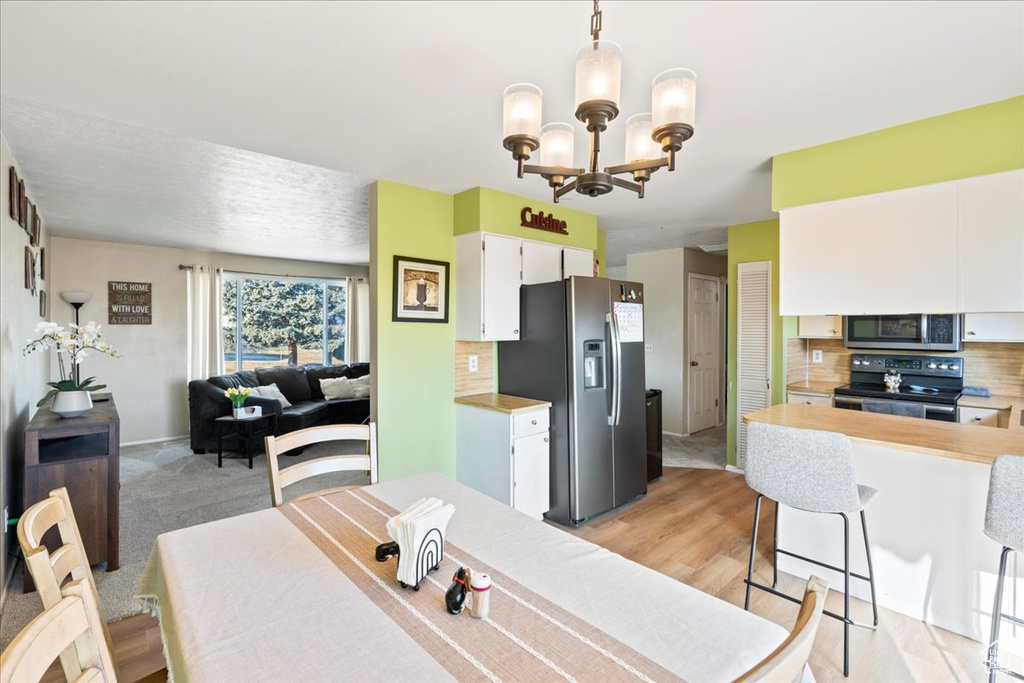 Kitchen featuring white cabinetry, stainless steel appliances, decorative backsplash, a notable chandelier, and decorative light fixtures