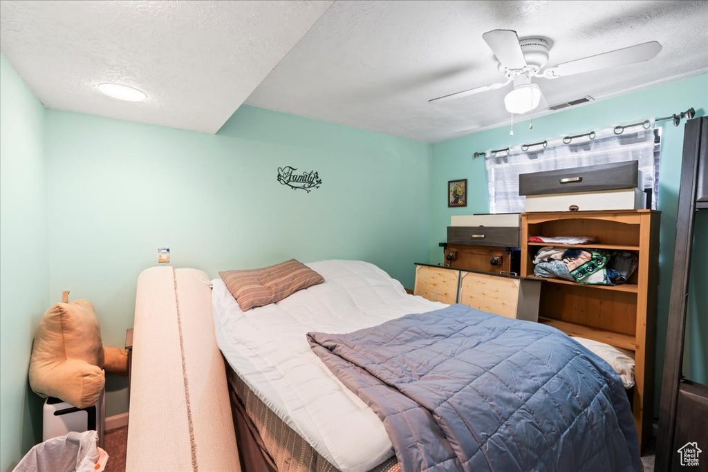 Carpeted bedroom featuring ceiling fan and a textured ceiling