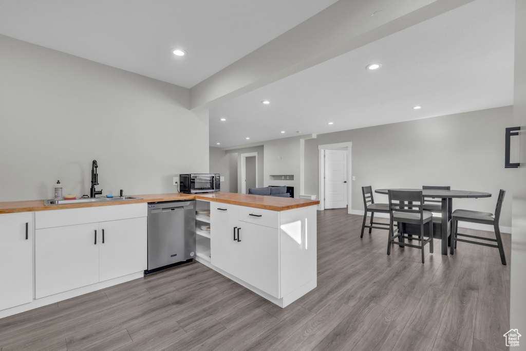 Kitchen with stainless steel dishwasher, white cabinets, wooden counters, and sink