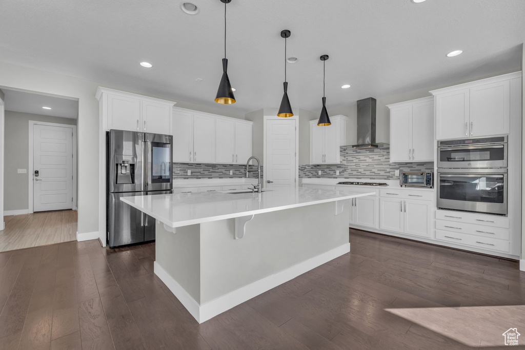 Kitchen with appliances with stainless steel finishes, wall chimney exhaust hood, and white cabinets