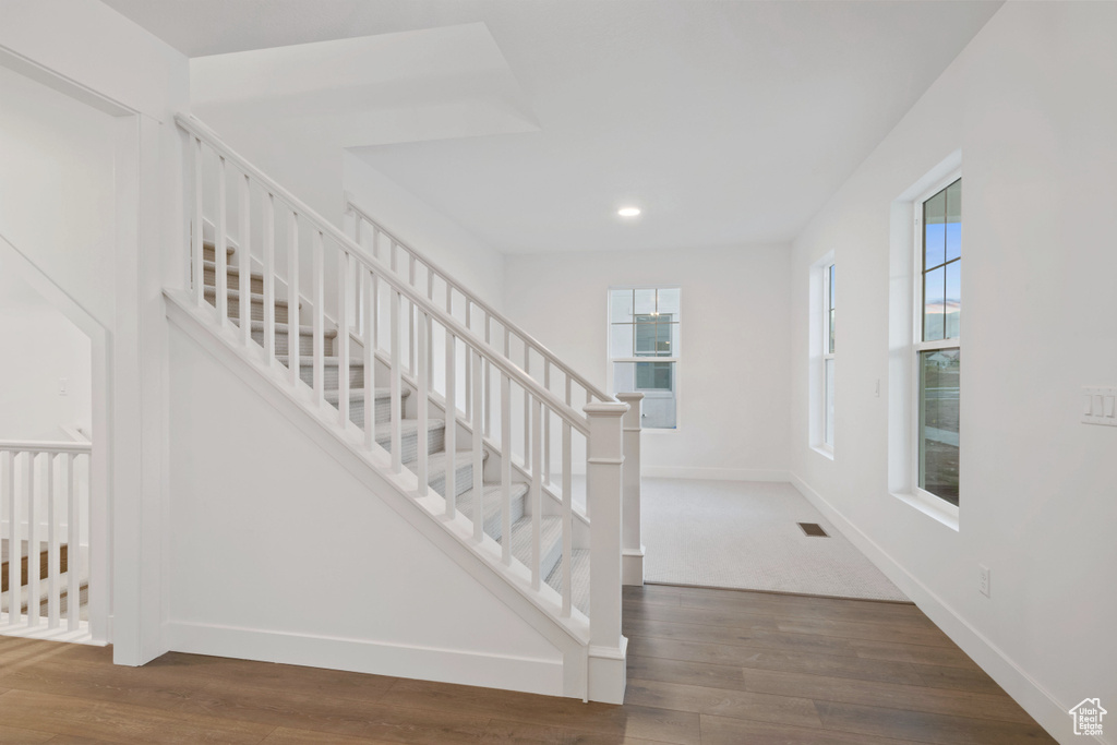 Stairway with plenty of natural light, wood finished floors, and recessed lighting