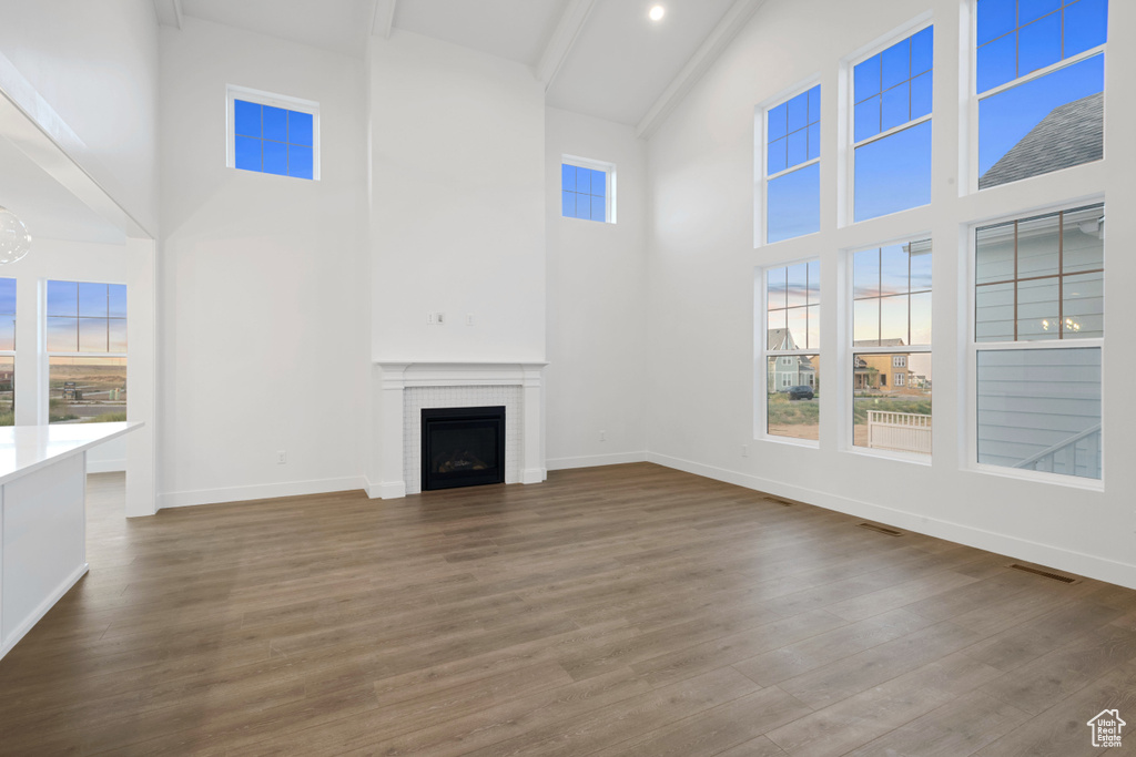 Unfurnished living room with a high ceiling, dark wood-style flooring, a fireplace, and beam ceiling
