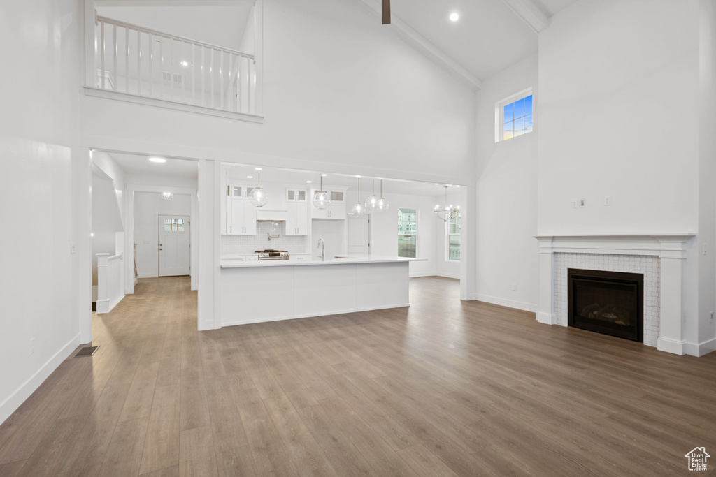 Unfurnished living room featuring high vaulted ceiling, healthy amount of natural light, wood finished floors, a tile fireplace, and a chandelier