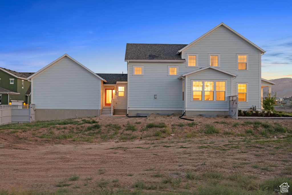 Back of property at dusk with entry steps and a shingled roof