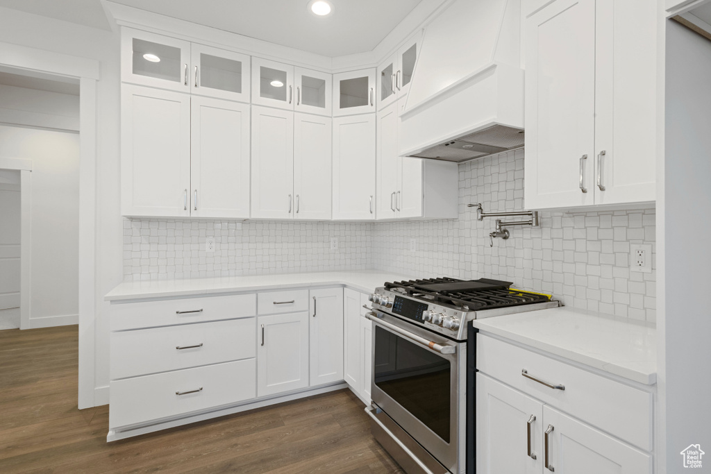Kitchen featuring stainless steel gas range oven, custom range hood, dark wood-style flooring, glass insert cabinets, and white cabinets