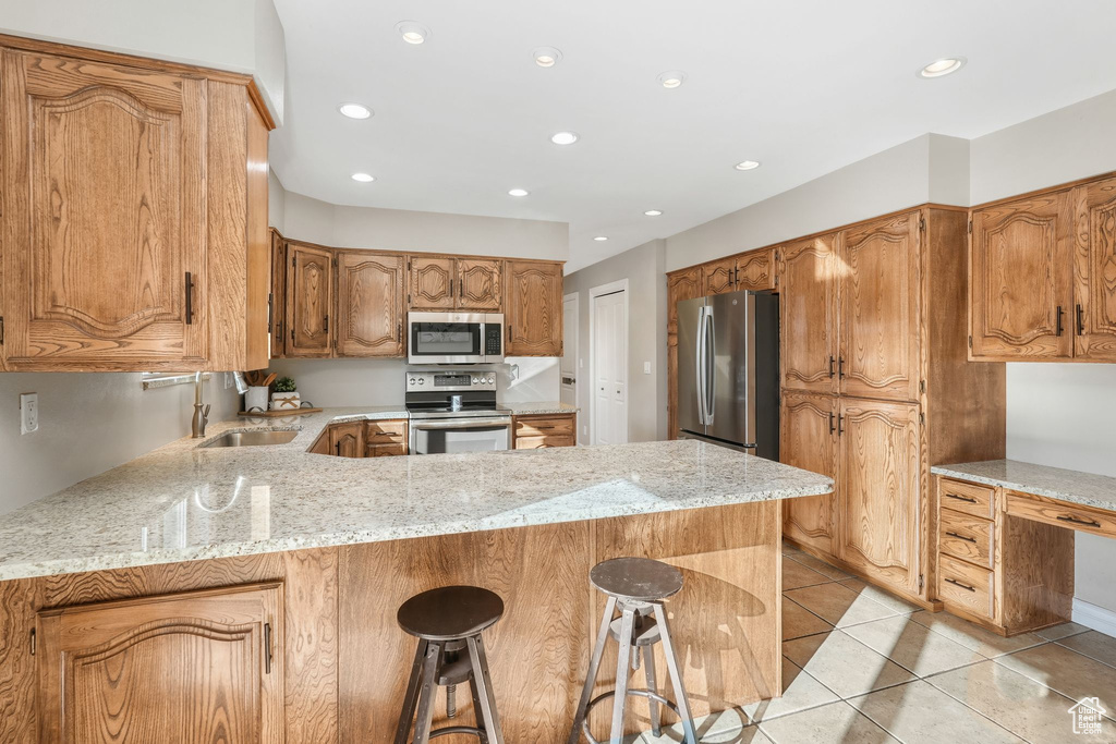 Kitchen featuring kitchen peninsula, sink, stainless steel appliances, light tile patterned floors, and light stone counters