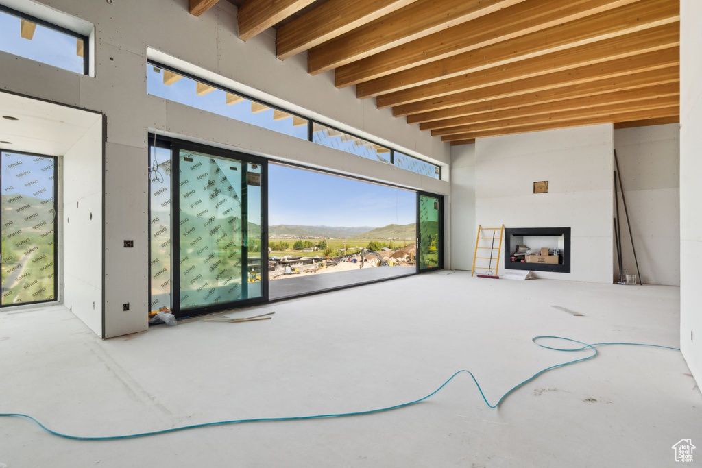 Unfurnished living room featuring a fireplace, beamed ceiling, a mountain view, and concrete flooring
