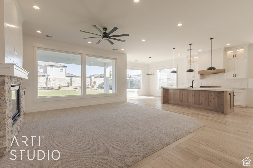 Unfurnished living room featuring ceiling fan, a stone fireplace, and light hardwood / wood-style flooring