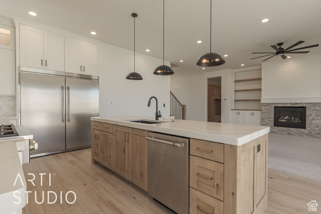 Kitchen with white cabinets, appliances with stainless steel finishes, decorative light fixtures, sink, and a center island with sink