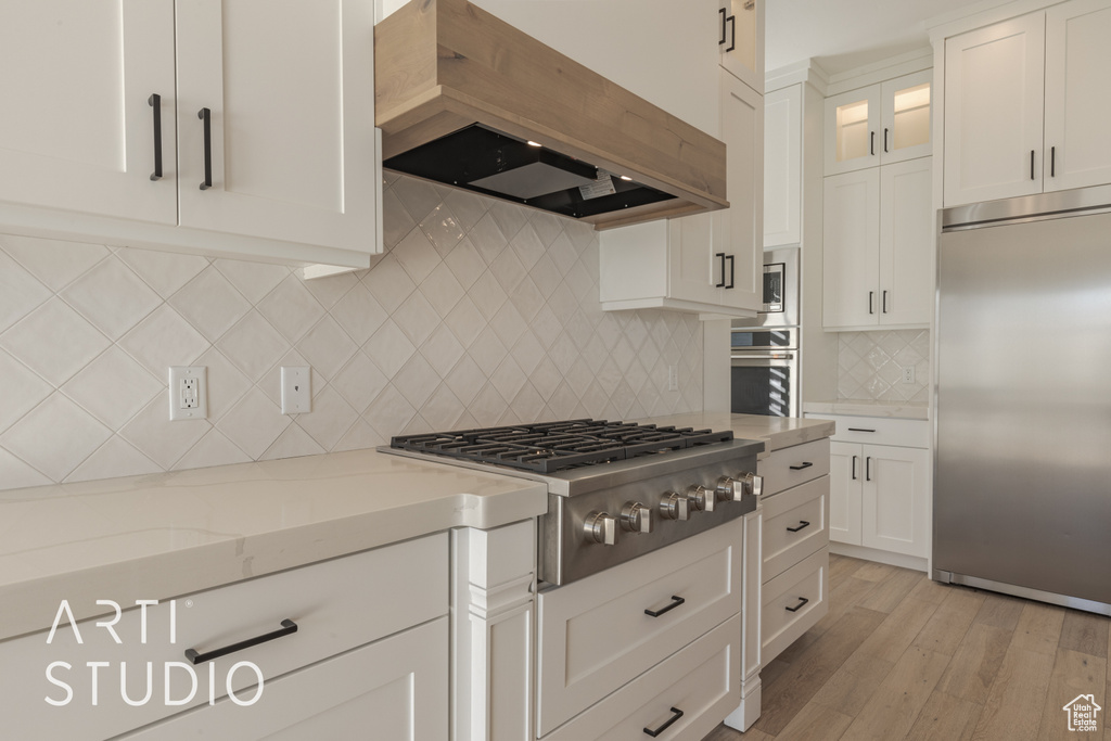 Kitchen featuring light stone countertops, white cabinets, built in appliances, decorative backsplash, and premium range hood