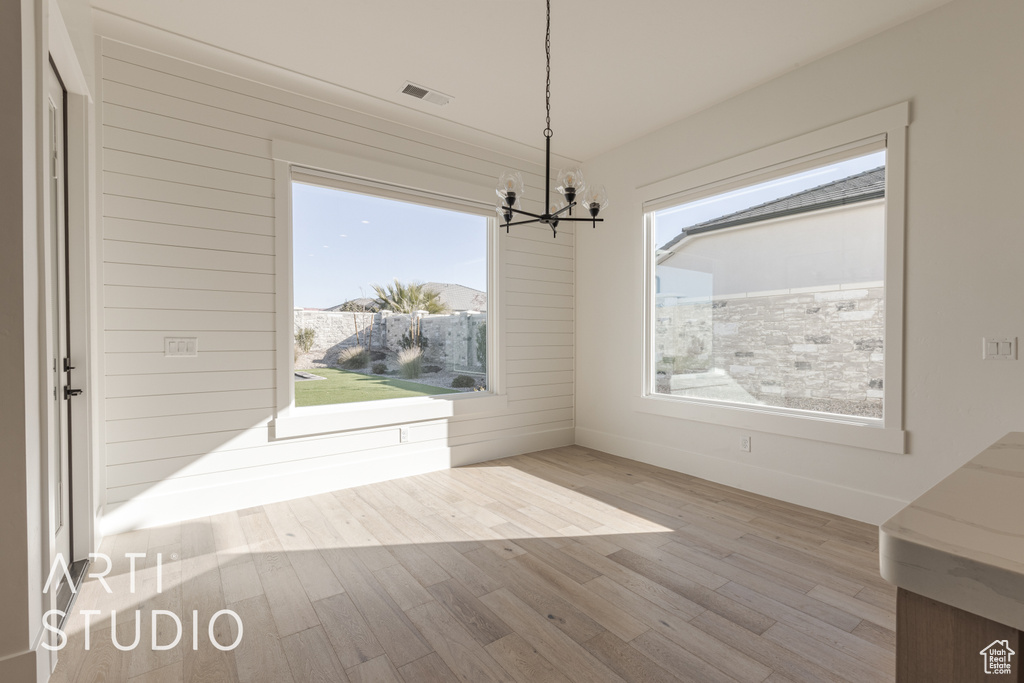 Unfurnished dining area with plenty of natural light, light wood-type flooring, and an inviting chandelier
