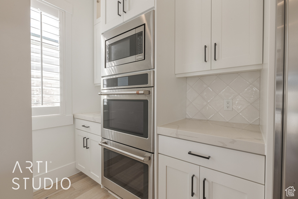 Kitchen with decorative backsplash, appliances with stainless steel finishes, a wealth of natural light, and light stone counters