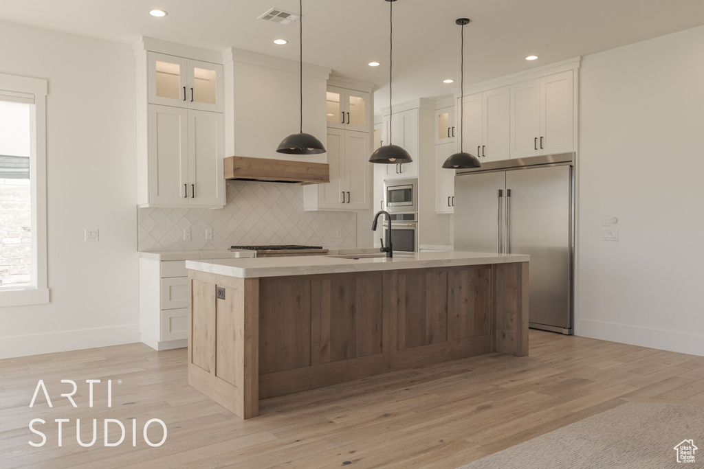 Kitchen with white cabinets, a kitchen island with sink, and built in appliances