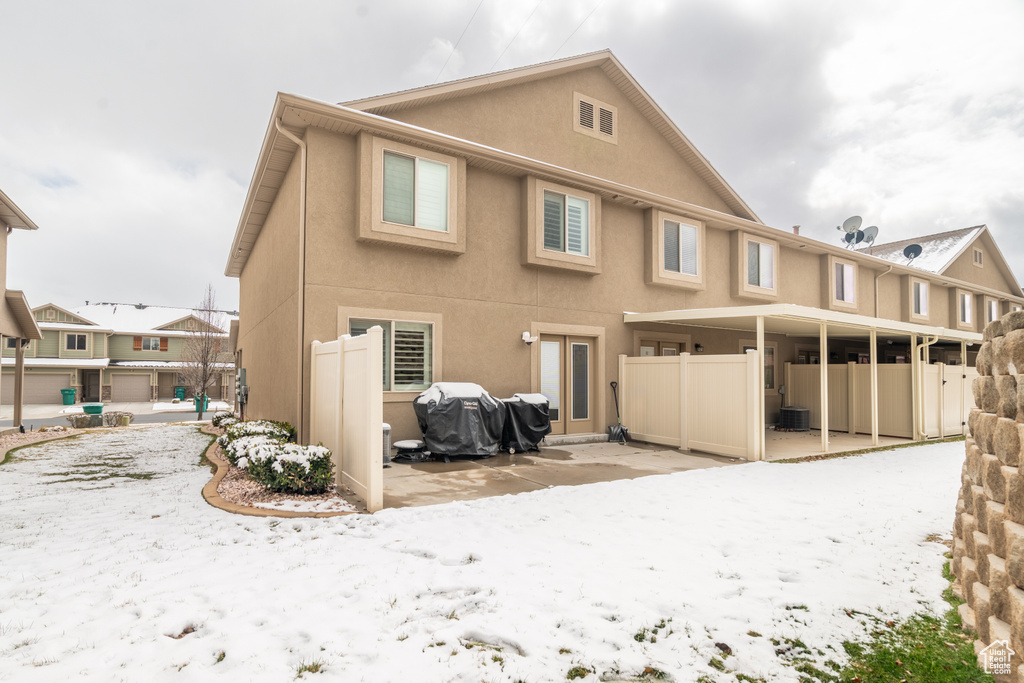 Snow covered house featuring a patio, fence, and stucco siding