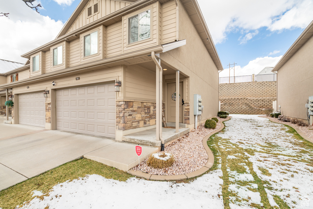 View of snowy exterior with a garage, stone siding, and driveway