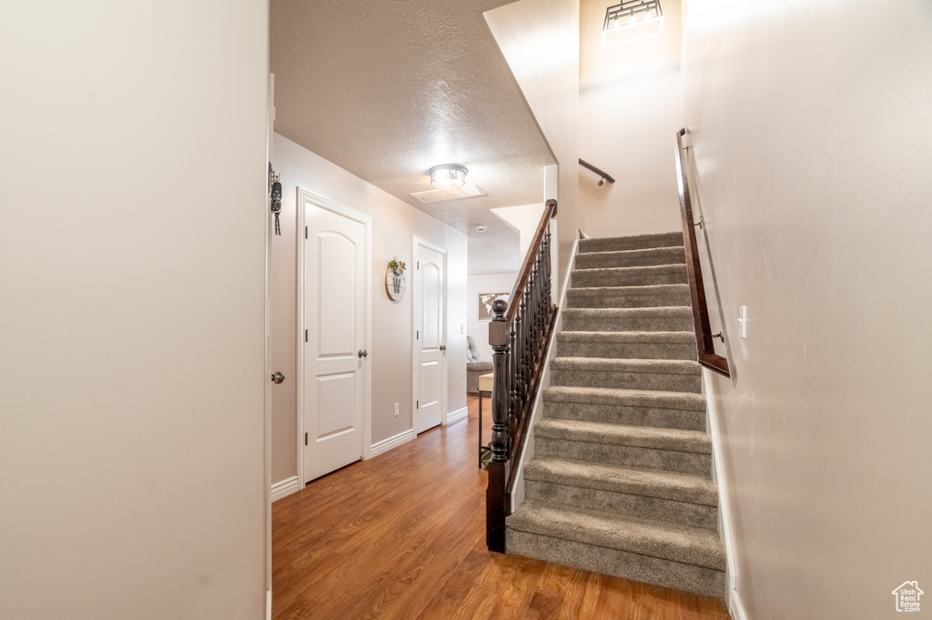 Staircase with visible vents, wood finished floors, baseboards, and a textured ceiling